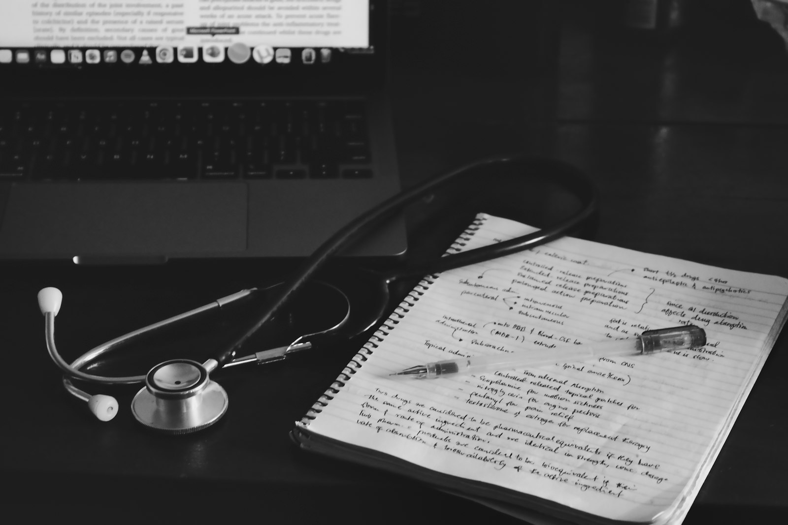 A notebook with a stethoscope resting beside a laptop